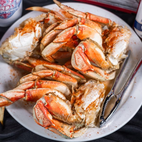 A plate of cooked crab legs and claws seasoned with spices, with hot sauce bottles nearby.