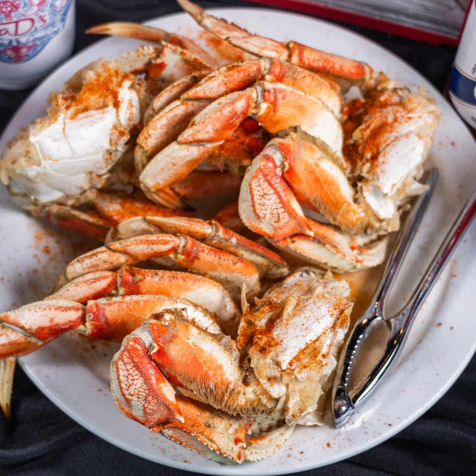 A plate of cooked crab legs and claws seasoned with spices, with hot sauce bottles nearby.