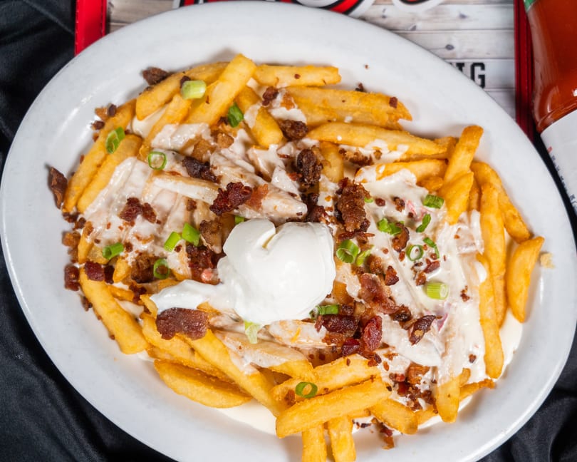 Loaded french fries topped with melted cheese, bacon bits, green onions, and a dollop of sour cream.