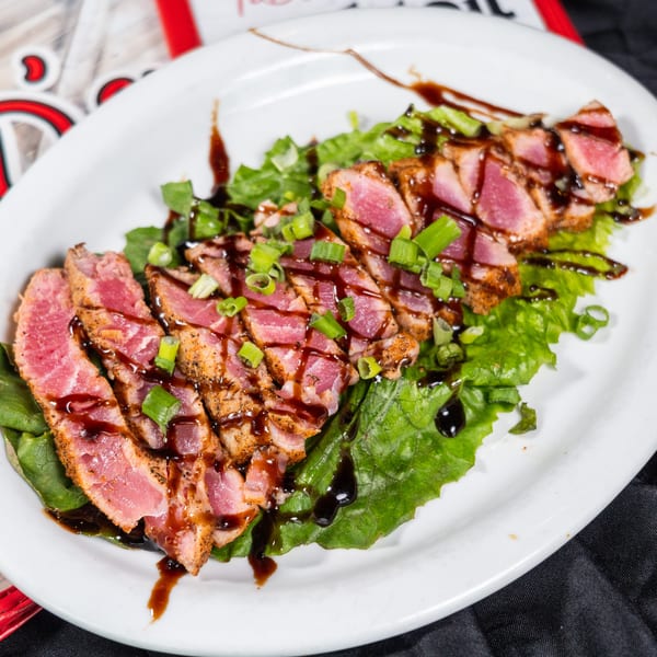 Seared tuna slices with green onions and balsamic glaze on a bed of lettuce.