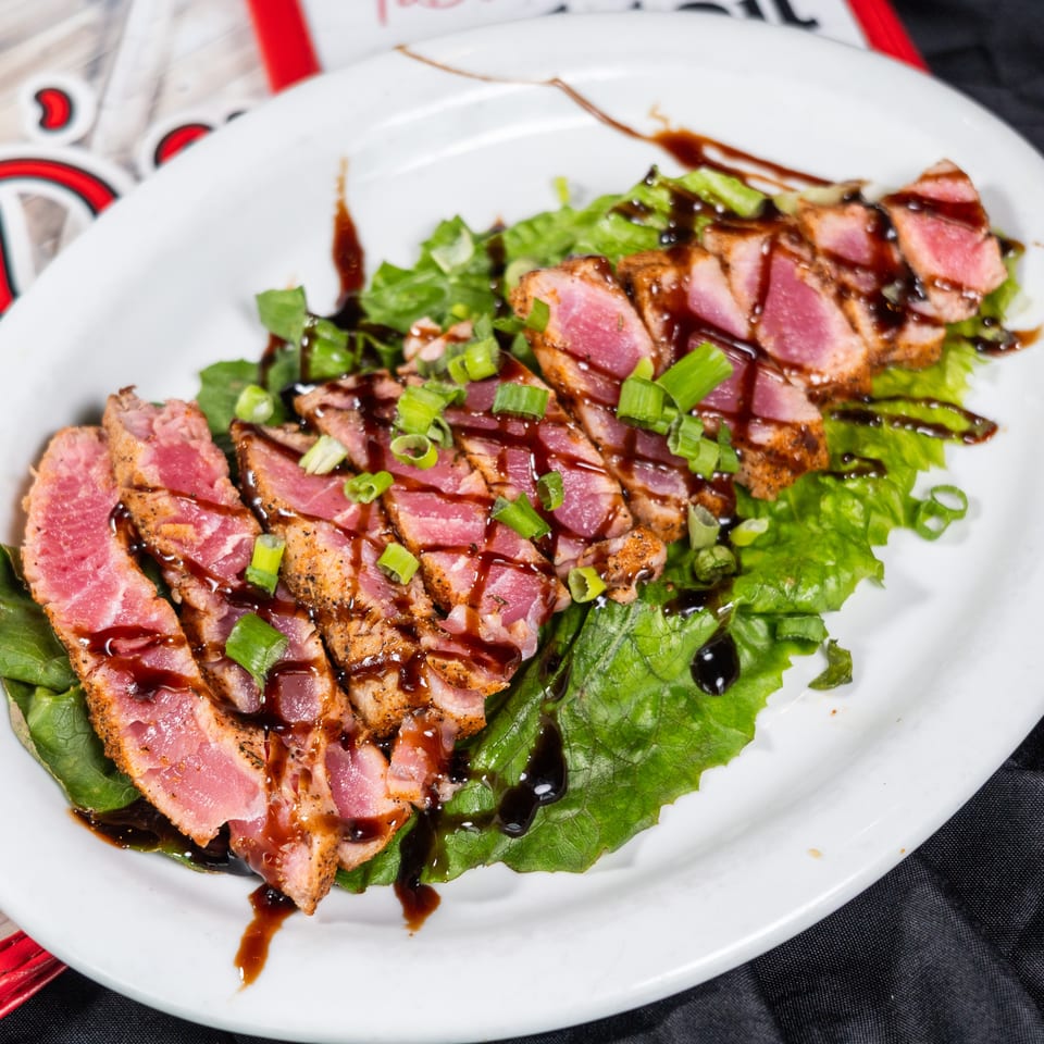 Seared tuna slices with green onions and balsamic glaze on a bed of lettuce.