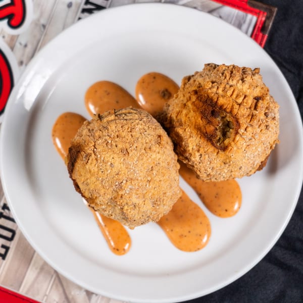 Two golden-brown fried hushpuppies with a creamy orange sauce drizzled on a white plate.