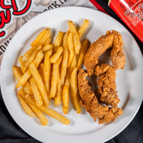 Crispy fried chicken tenders and golden french fries on a white plate, with seasoning cans nearby.