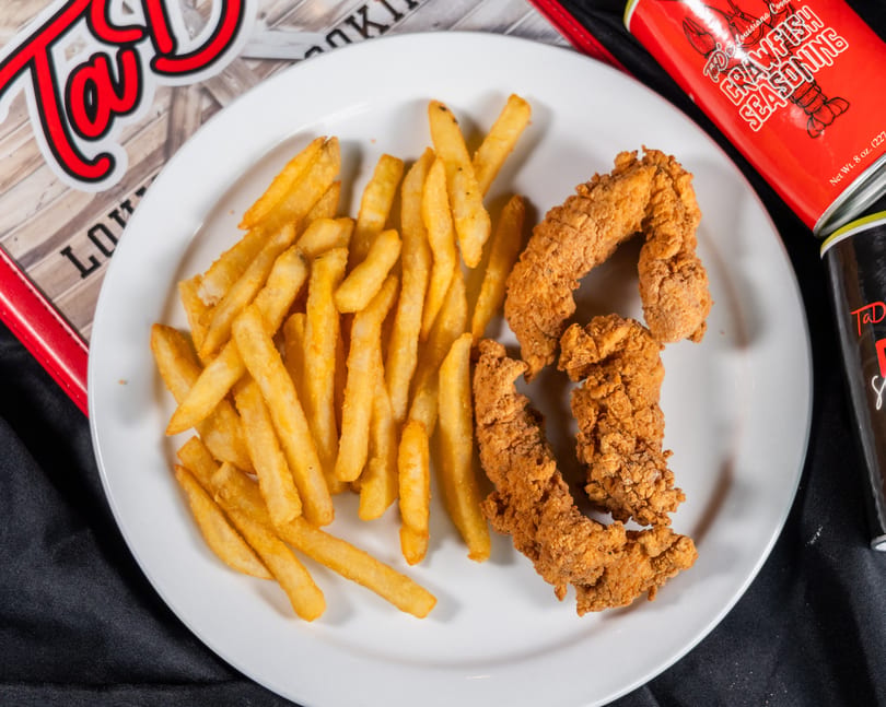 Crispy fried chicken tenders and golden french fries on a white plate, with seasoning cans nearby.