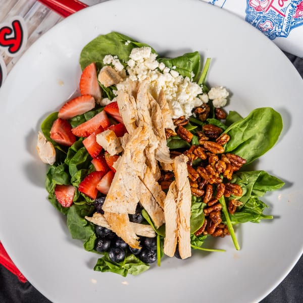 A vibrant salad with spinach, grilled chicken, strawberries, blueberries, pecans, and feta cheese.
