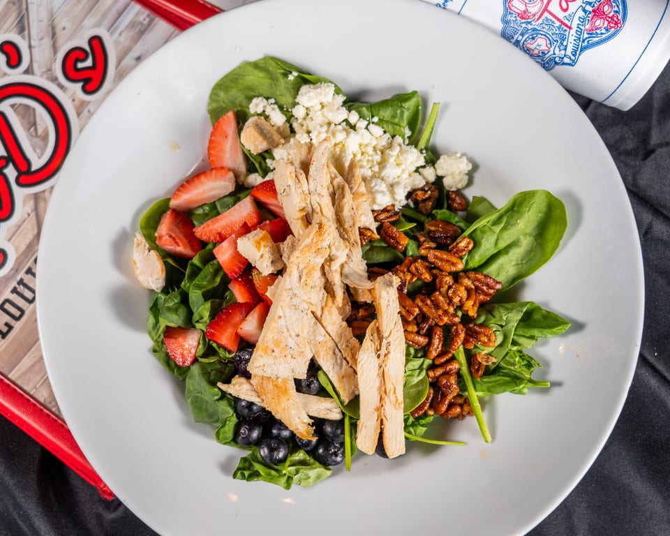 A vibrant salad with spinach, grilled chicken, strawberries, blueberries, pecans, and feta cheese.