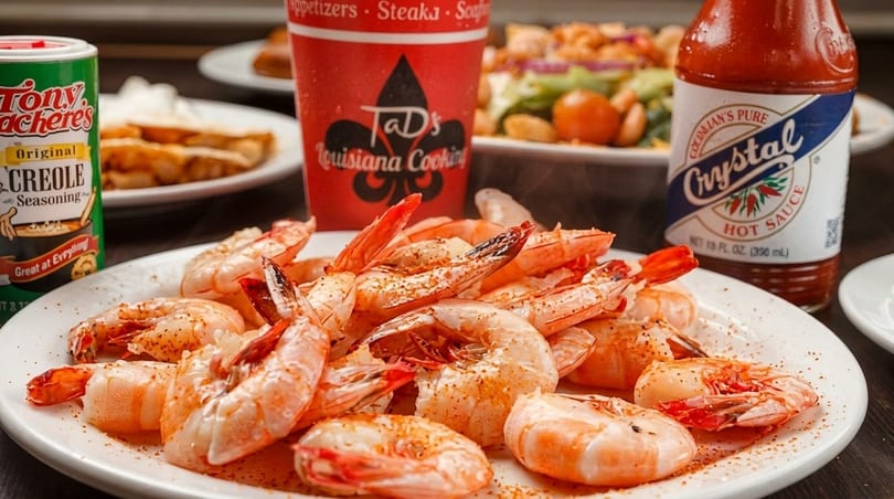 A plate of seasoned shrimp with Tony Chachere's Creole Seasoning and Crystal Hot Sauce in the background.
