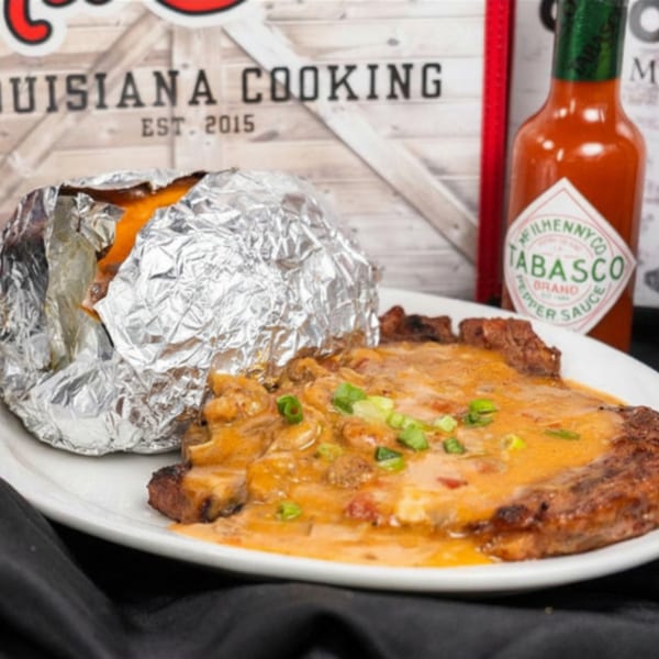Steak covered in creamy sauce and green onions, with a foil-wrapped baked potato and hot sauce.