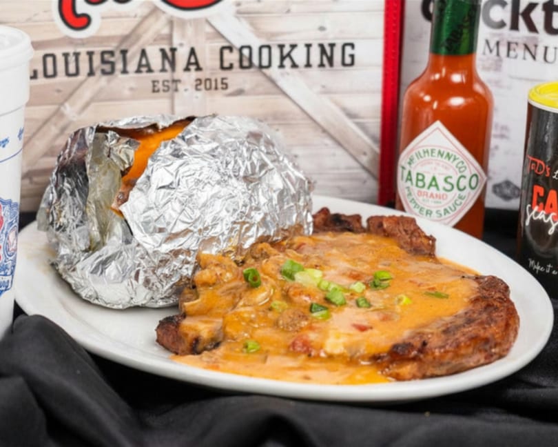 Steak covered in creamy sauce and green onions, with a foil-wrapped baked potato and hot sauce.