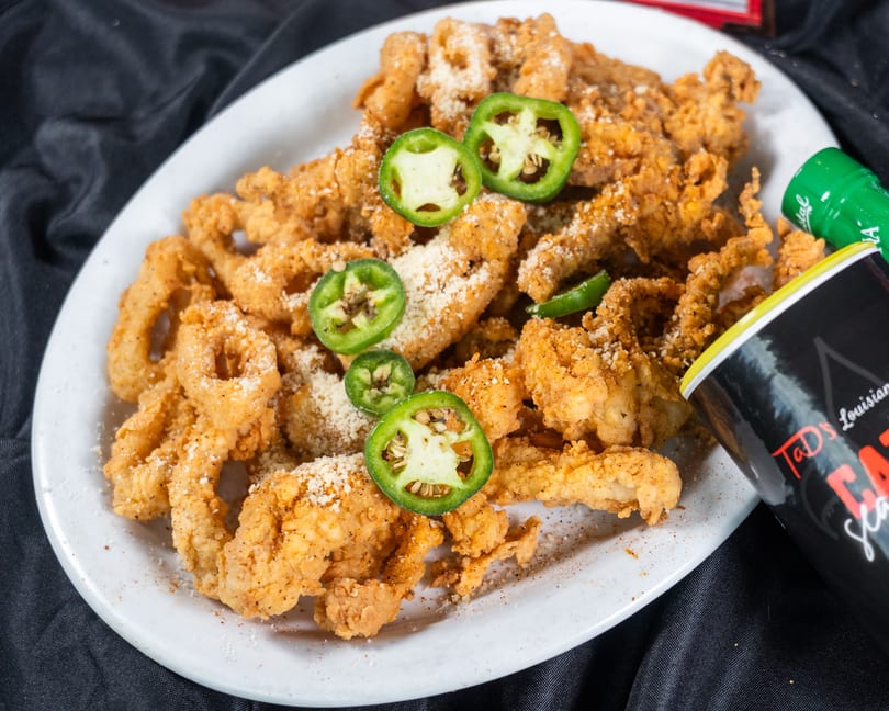 Fried calamari and shrimp with jalapeños and parmesan cheese, next to a bottle of Tad's Louisiana seasoning.