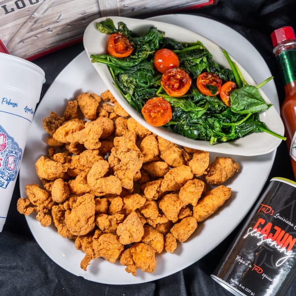 Fried chicken, spinach with tomatoes, a drink, Tabasco, and Cajun seasoning on a black cloth.