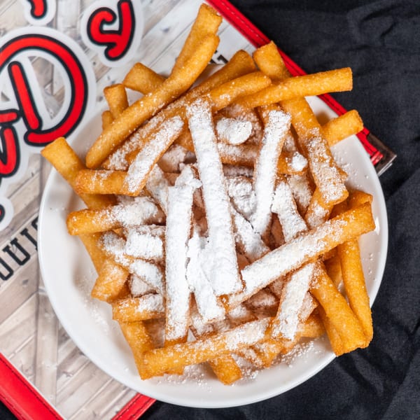 A white plate filled with golden-brown french fries, heavily dusted with powdered sugar.