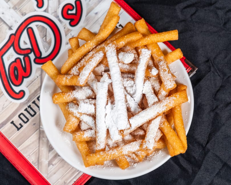 A white plate filled with golden-brown french fries, heavily dusted with powdered sugar.