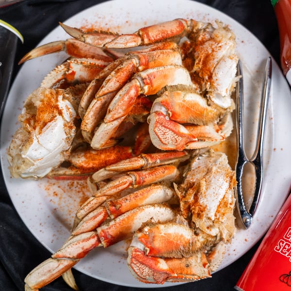 A plate of seasoned crab legs with a crab cracker, hot sauce, and seasoning containers.