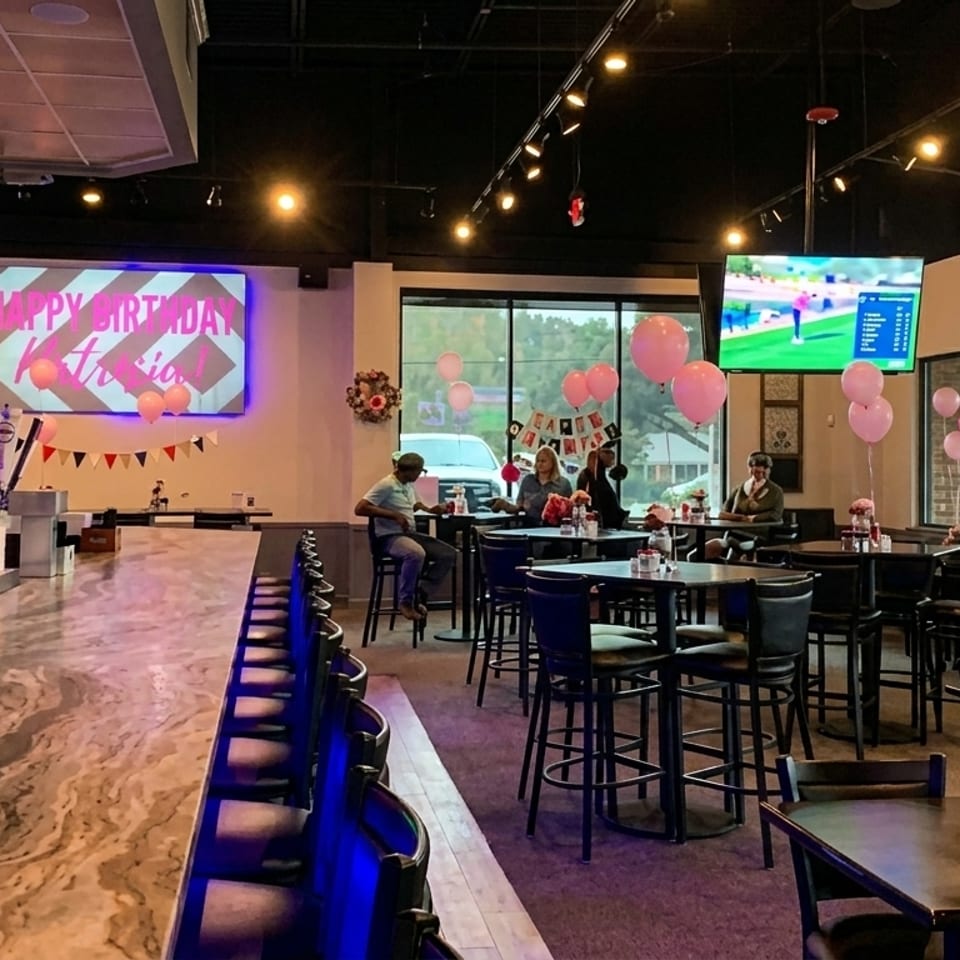 A restaurant bar area with a long counter, high-top tables, and pink balloons for a birthday.