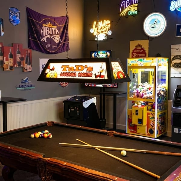 A game room with a pool table, arcade games, and neon signs on the wall.