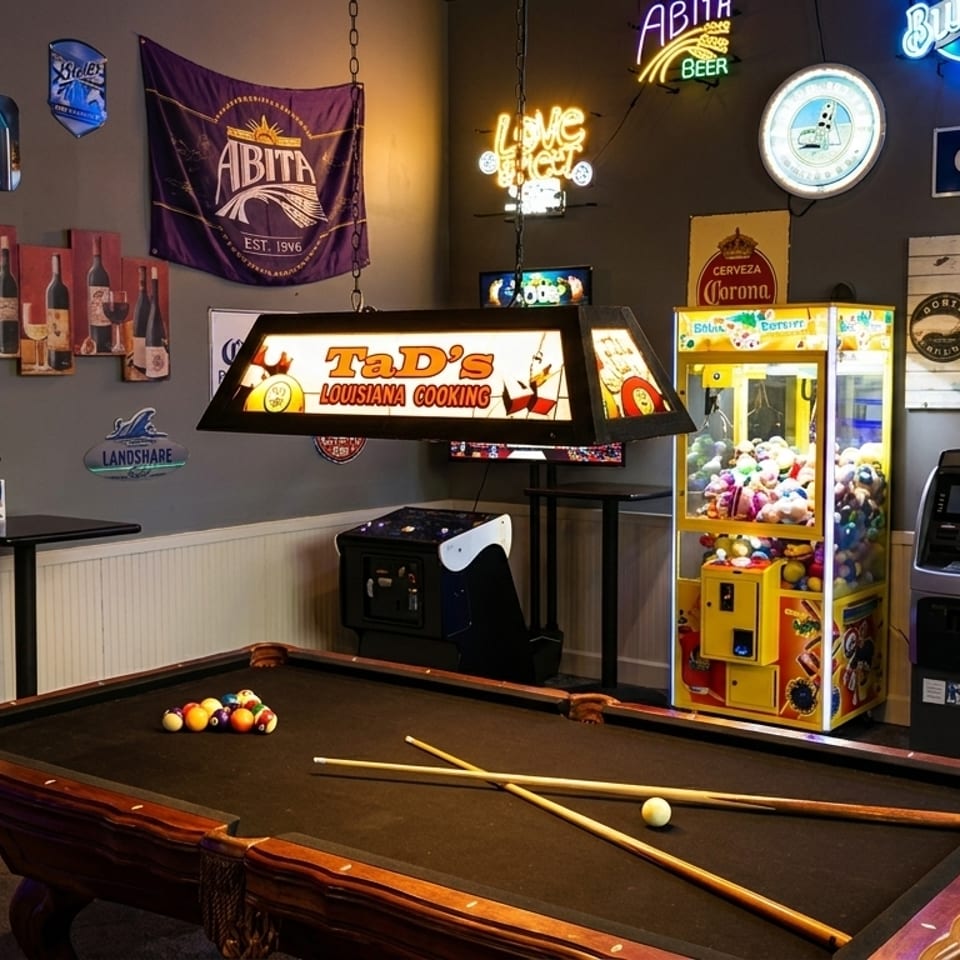 A game room with a pool table, arcade games, and various beer and restaurant signs on the walls.