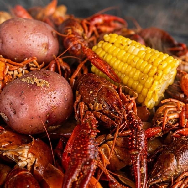 Close-up of a steaming pile of boiled crawfish, red potatoes, and corn on the cob.
