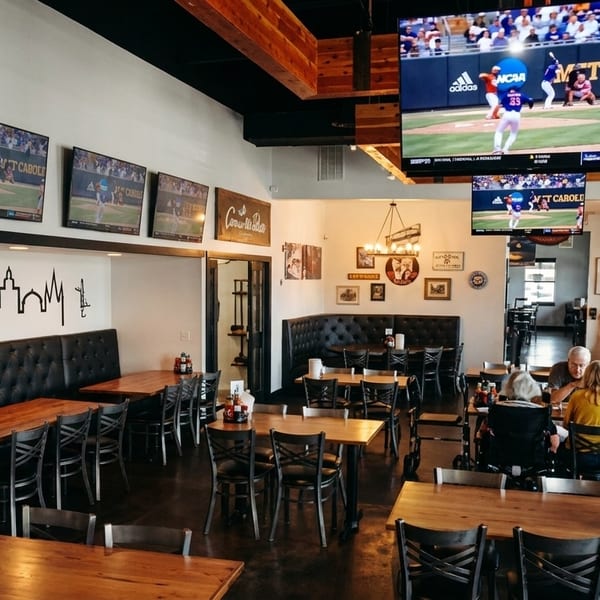 A spacious restaurant interior with multiple TVs showing baseball, featuring wooden tables, black booths, and diners.