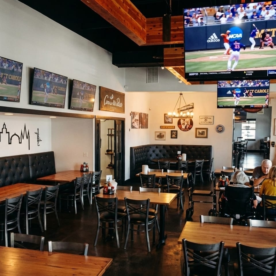A spacious restaurant interior with multiple TVs showing baseball, featuring wooden tables, black booths, and diners.