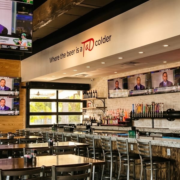 A sports bar interior with multiple TVs showing sports, a long bar, and dining tables.