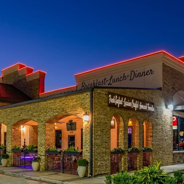 Tad's Louisiana Cooking restaurant exterior at dusk, with red neon lights illuminating the brick facade and arched patio.