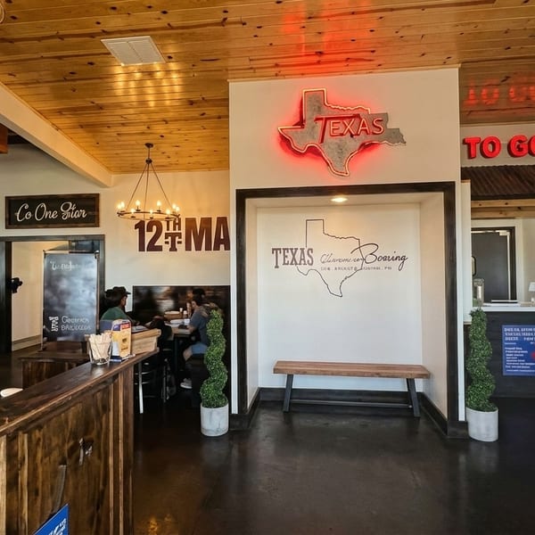 Interior of a Texas-themed restaurant with wooden accents, neon signs, and a dining area.